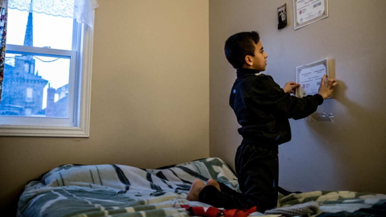 Basel Alrashdan, 11, tapes achievement certificates from school and community events to his bedroom wall in Charlottetown, Canada