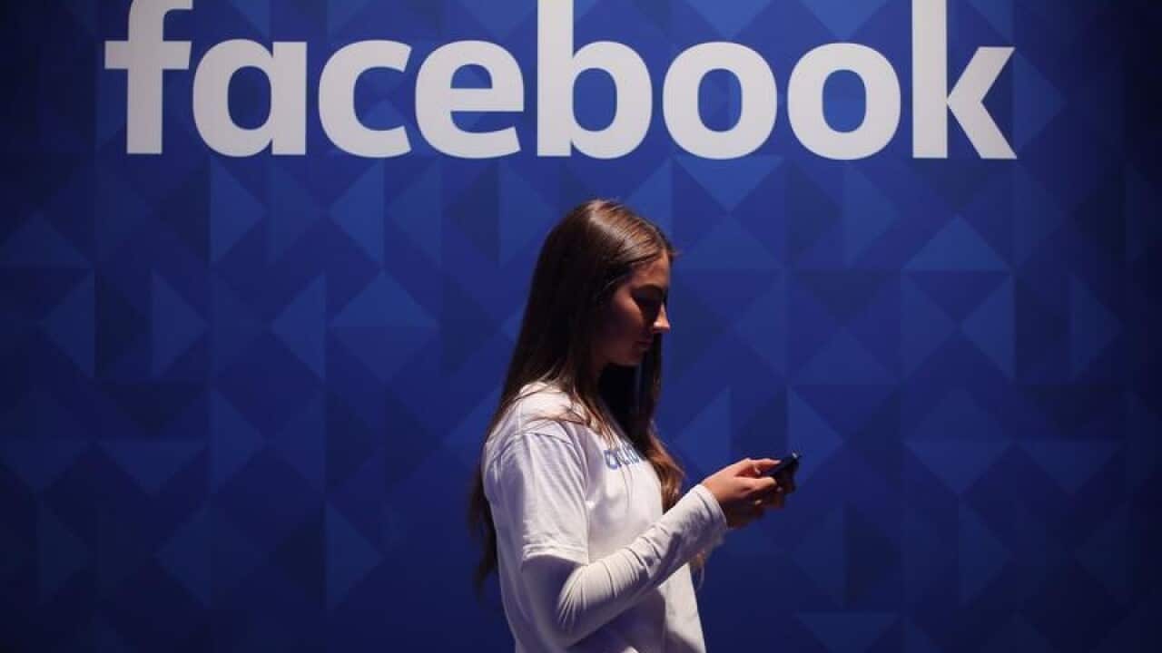 A woman using her phone under a Facebook logo