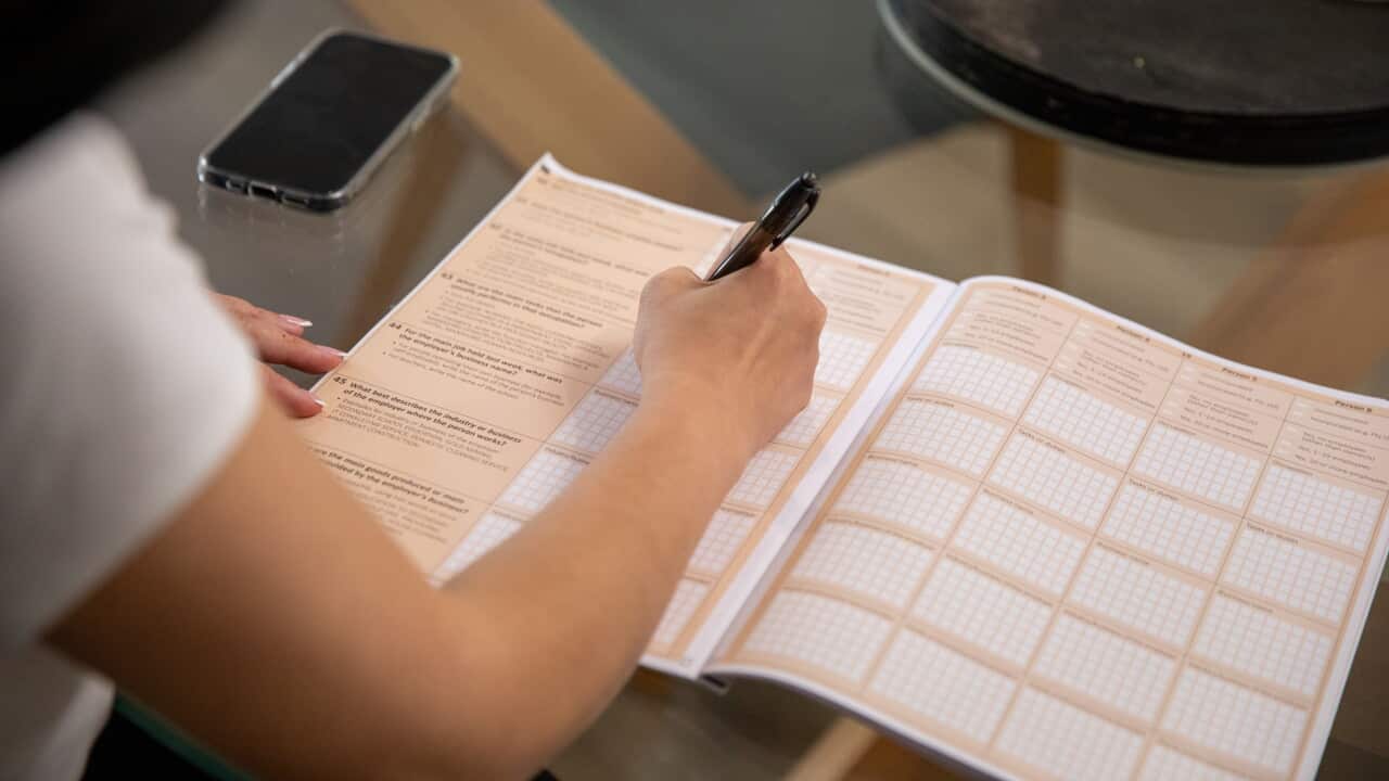 A4 Census booklet open on table, as a women uses a pen to fill in the form.