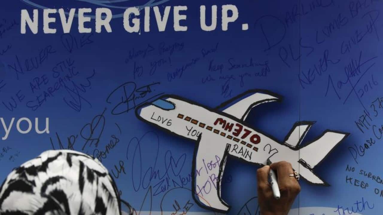 A woman writes messages on a banner for missing flight MH370.