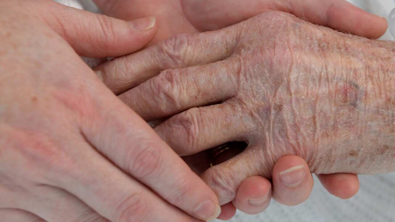 A nurse holds the hand of an elderly patient in a hospital