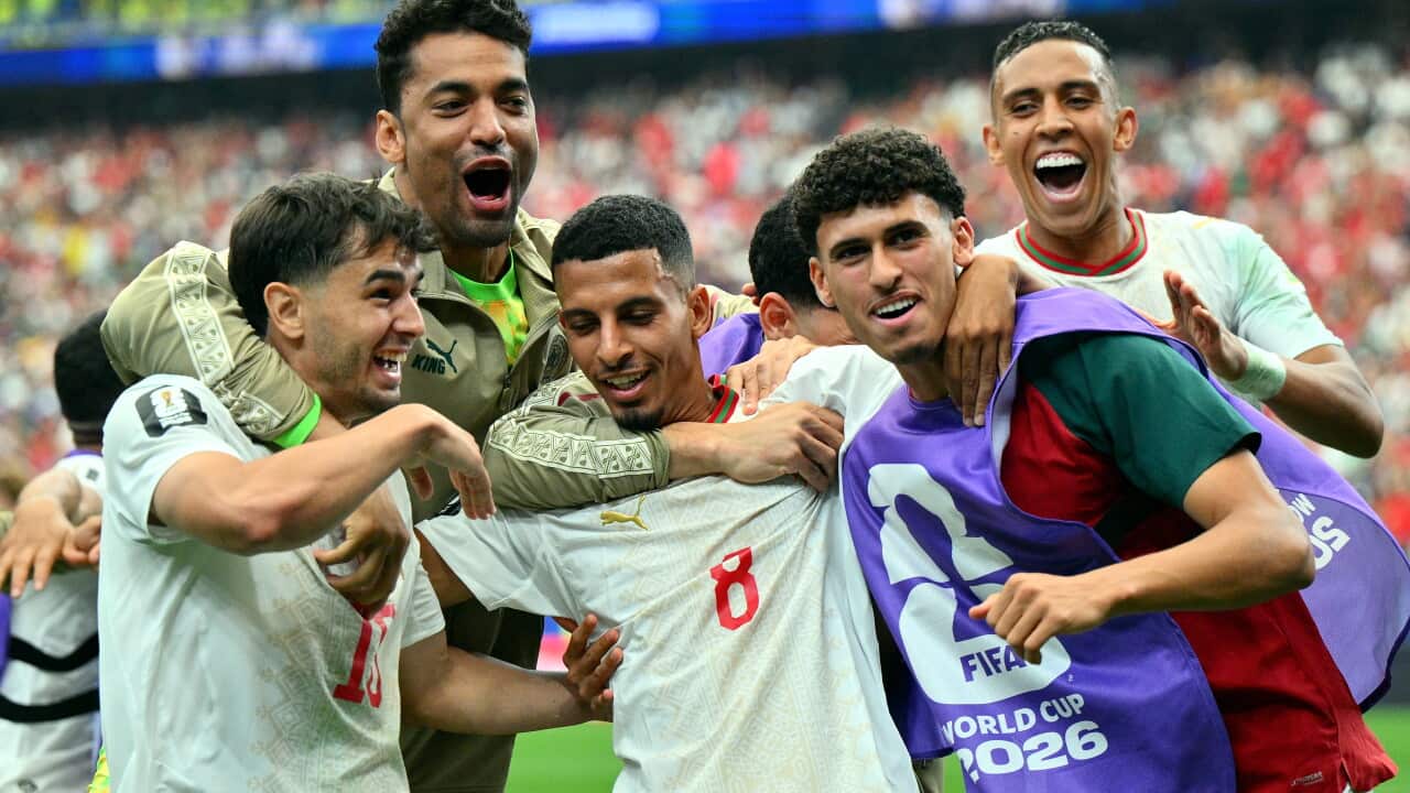 A football player in a white jersey celebrates a goal surrounded by his teammates.