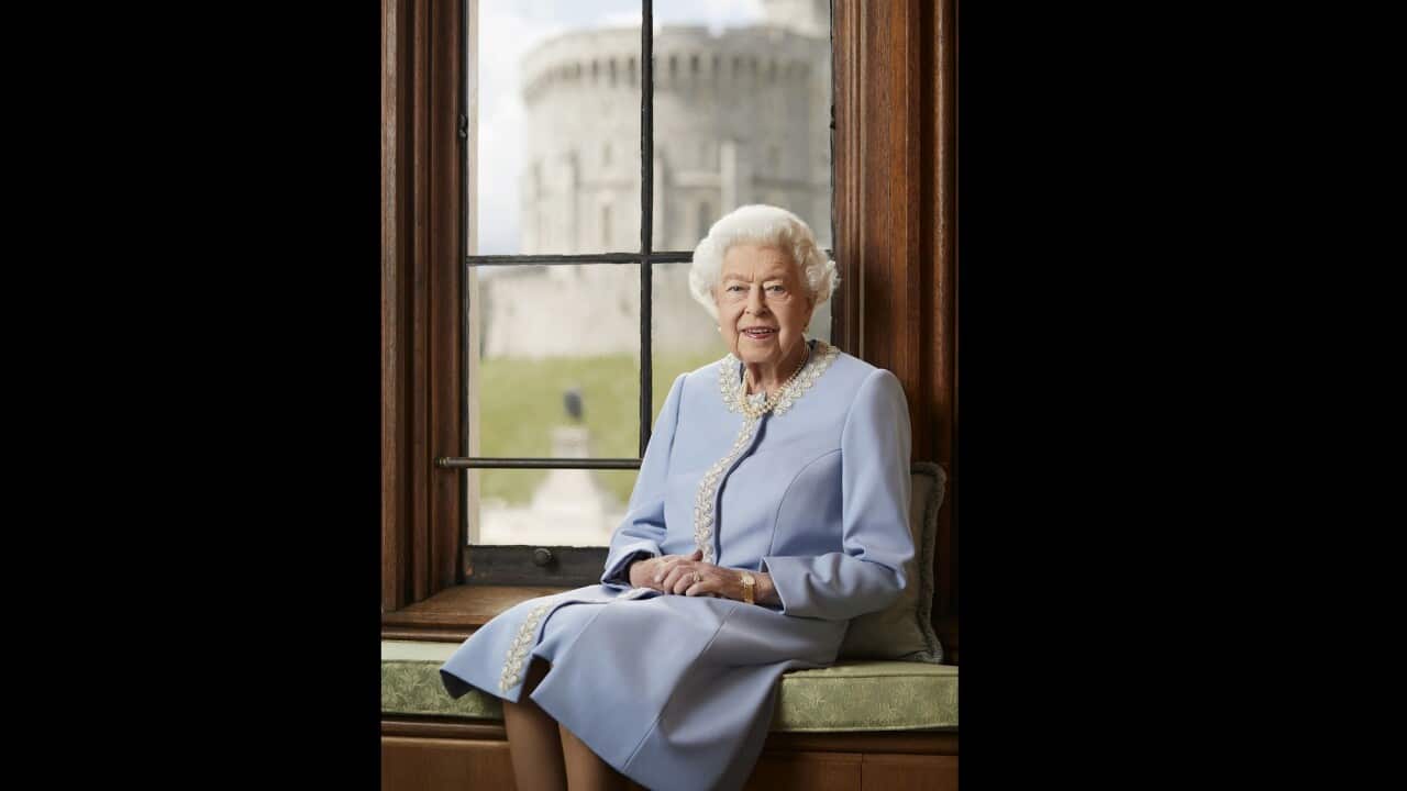 Queen Elizabeth II dressed in pale blue outfit seated near window for her official portrait.