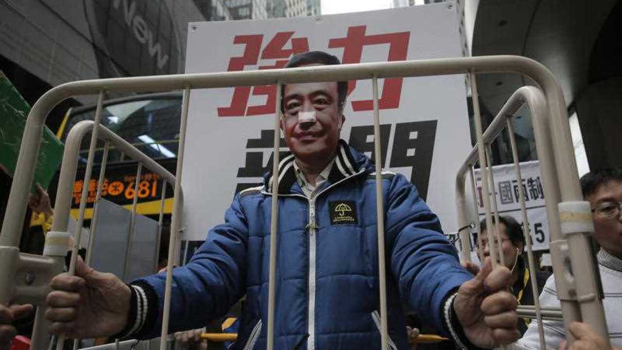 A protester wearing a mask of missing bookseller Lee Bo sits in a cage during a protest against the disappearances of booksellers in Hong Kong, Sunday, Jan. 10, 2016. (AAP)