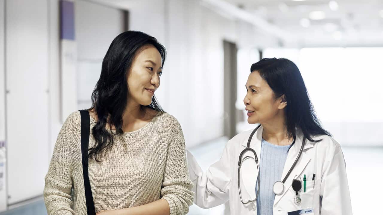 A smiling woman doctor talking to woman in a hospital corridor