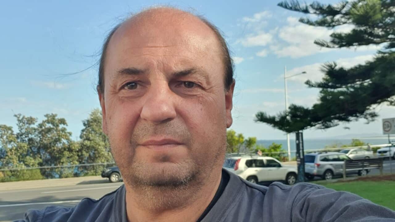 A middle aged man in a t-shirt standing outside in a public park.