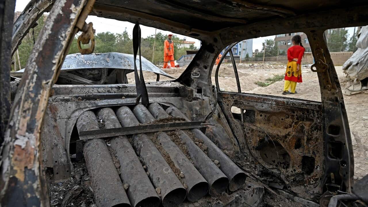 A girl stands next to a damaged car in Kabul