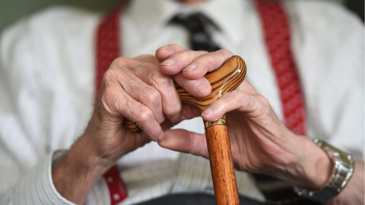 A close up of an elderly man's hands placed on his walking stick