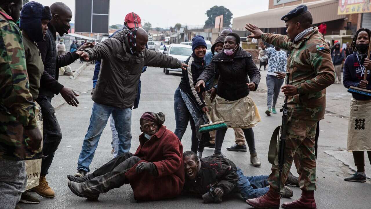 A soldier stops community members from attacking two men accused of looting.