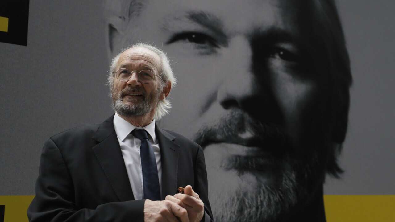 Julian Assange's biological father John Shipton standing in front of a poster of his son in London.