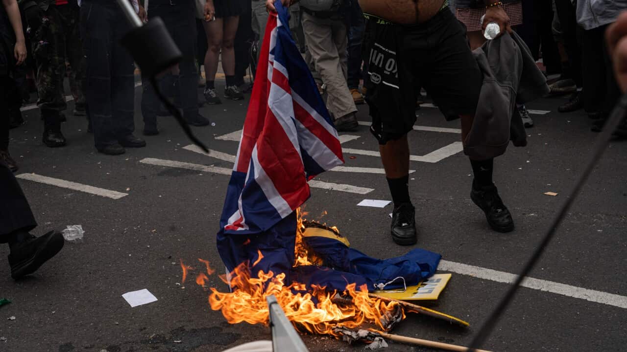 The lower half of a man holding a burning Australian flag