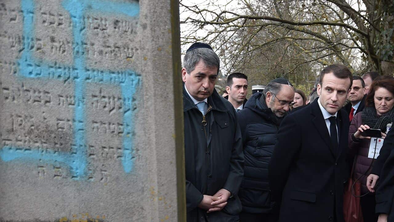 TOPSHOT - French President Emmanuel Macron looks at a grave vandalised with a swastika during a visit at the Jewish cemetery in Quatzenheim, on February 19, 2019, on the day of a nationwide marches against a rise in anti-Semitic attacks. - Around 80 grave