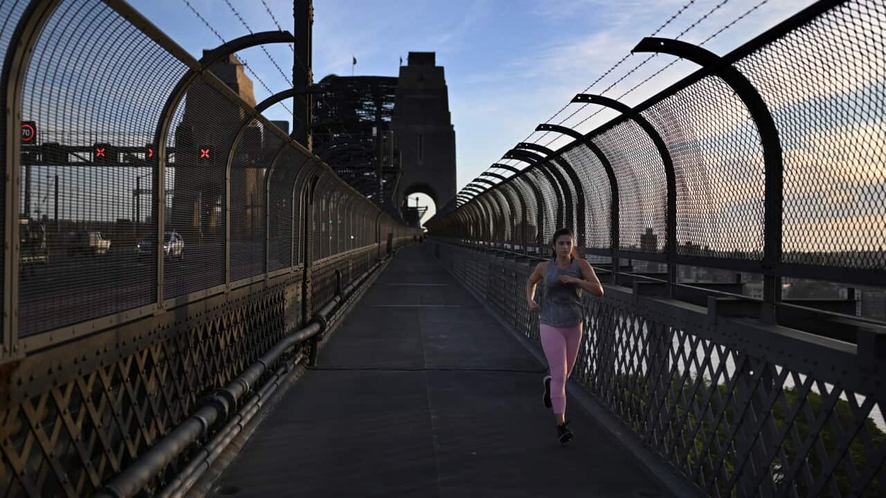 A woman jogs over the Sydney Harbour Bridge at sunrise