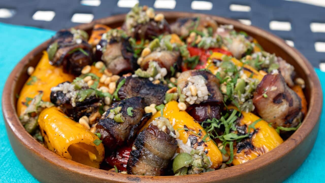 A shallow round brown wooden bowl holds a bacon and mini capsicum salad. It sits on a vibrant blue cloth.