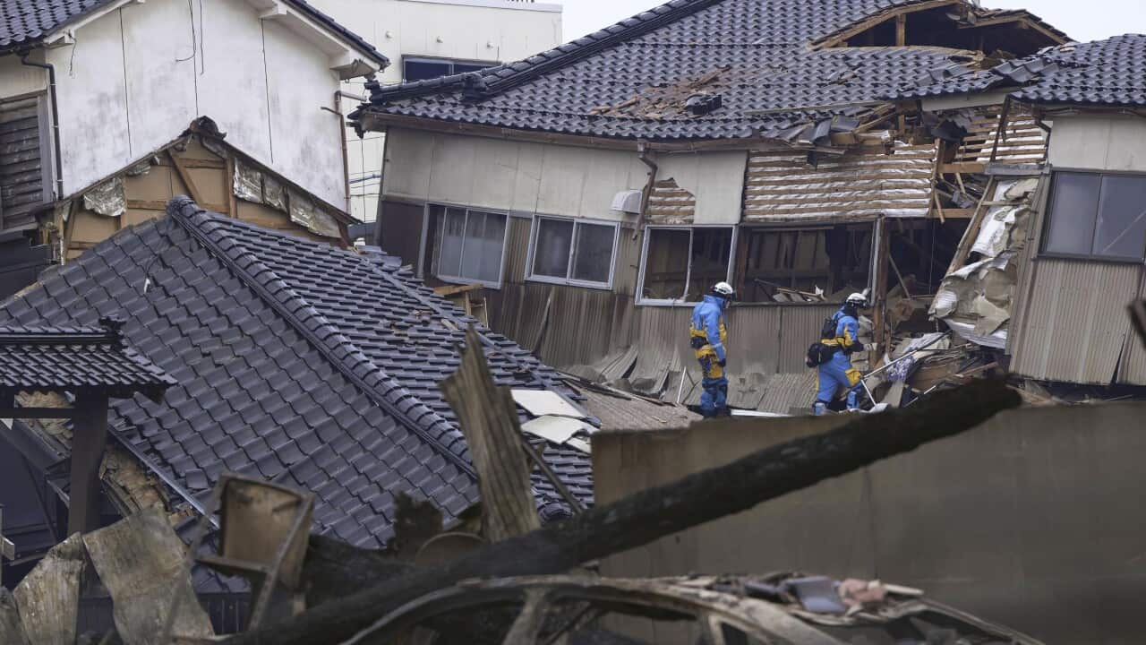 Two people walk on toppled houses, debris.