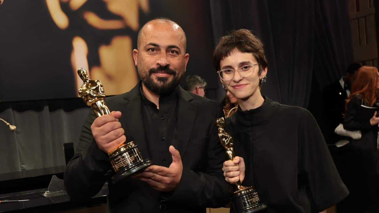 A man and a woman pose for a photo, both holding Oscar trophies in their hands.