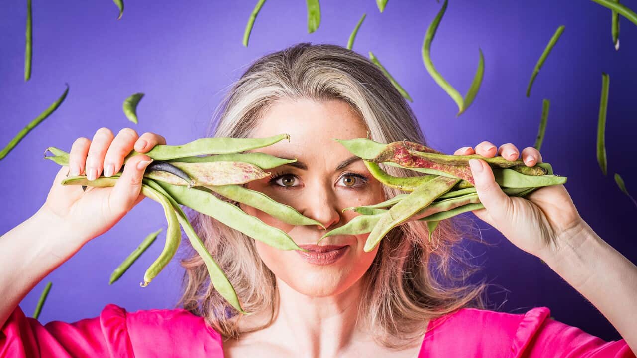 Ali Honour in a bright pink shirt holds handfuls of bean pods in front of her face.