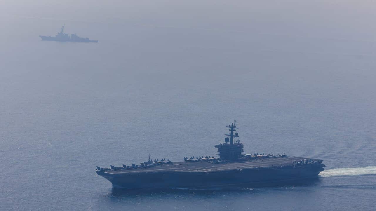 A large aircraft carrier laden with fighter jets sails with a battleship across a calm sea.