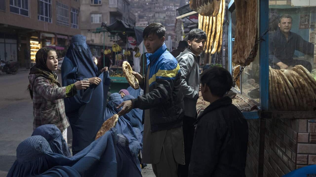 Un uomo distribuisce il pane alle donne afghane che indossano il burka fuori da una panetteria a Kabul, in Afghanistan. Dicembre 2021
