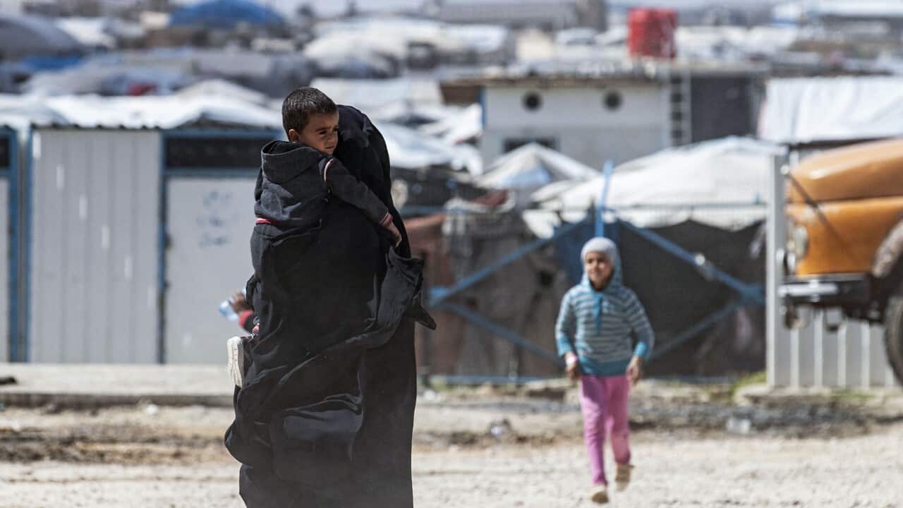 A woman wearing a niqab carries a baby boy in a camp