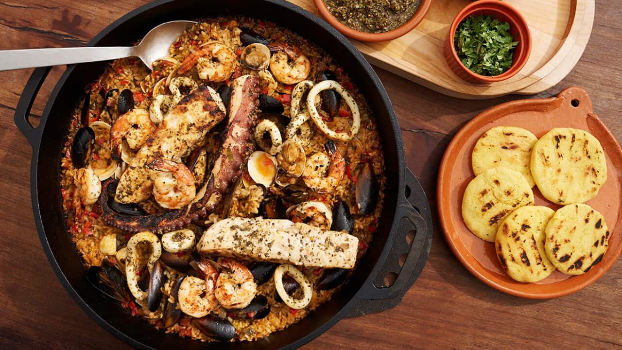 A black cast iron dish, seen from overhead, holds a seafood and rice stew.