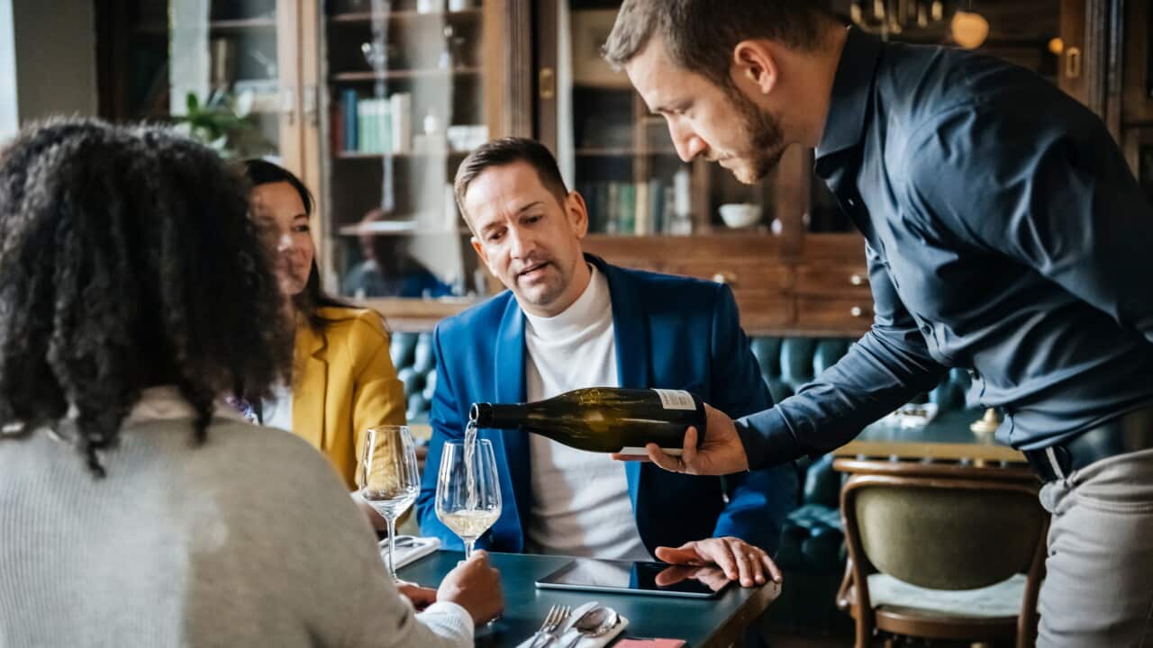 A waiter delicately pouring some white wine for a group of customers in a fancy restaurant.