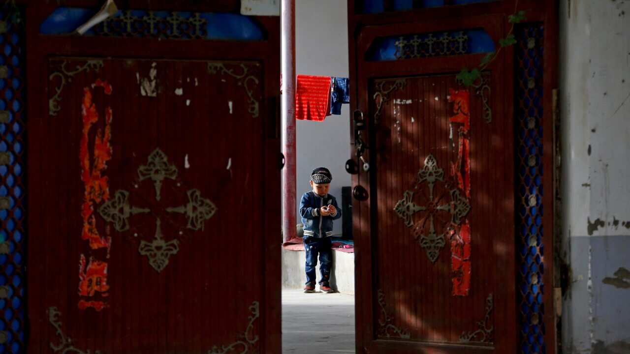 A Uighur child plays alone in the courtyard of a home at the Unity New Village in Hotan, in western China's Xinjiang region.