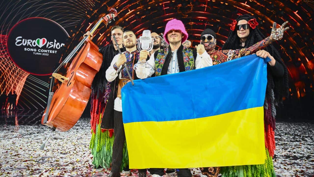 People gather together on stage full of confetti, carrying a blue and yellow (Ukrainian) flag
