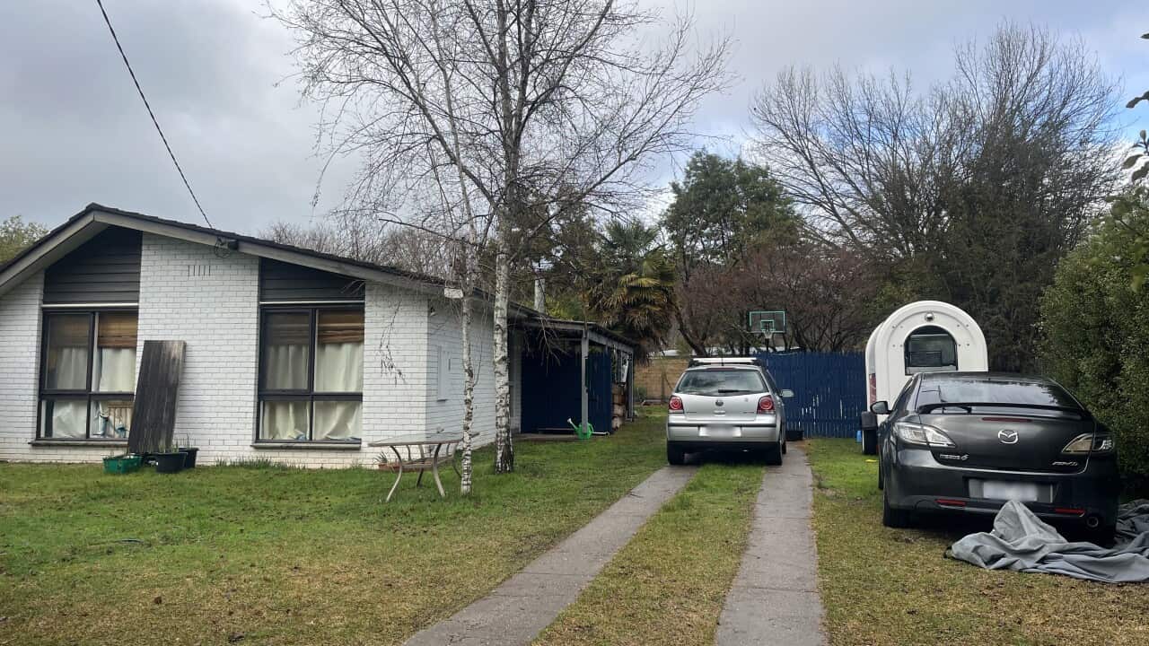 A white house, with two vehicles parked on the lawn near it.