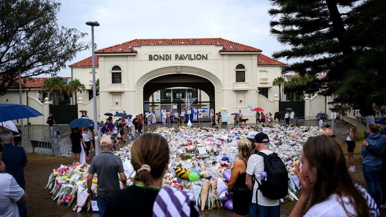 Flowers and other tributes on the ground outside Bondi Pavilion, where people are gathered.