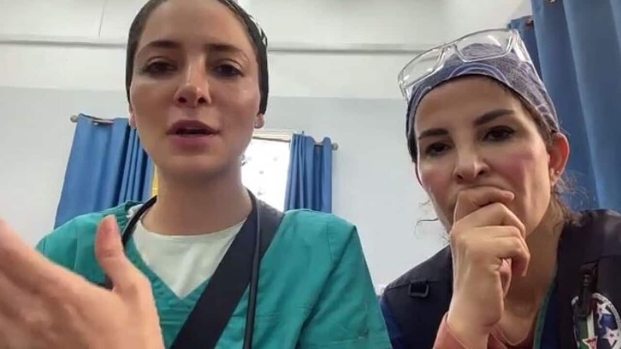 Two doctors in scrubs look at the camera barrel