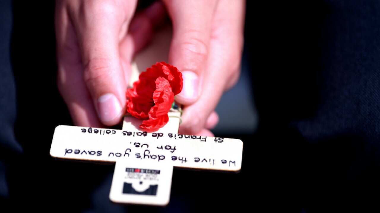 A boy holds a cross and a poppy in hands during a Remembrance Day ceremony at the Australian War Memorial in Canberra, Saturday, November 11, 2017. (AAP Image/Lukas Coch) NO ARCHIVING
