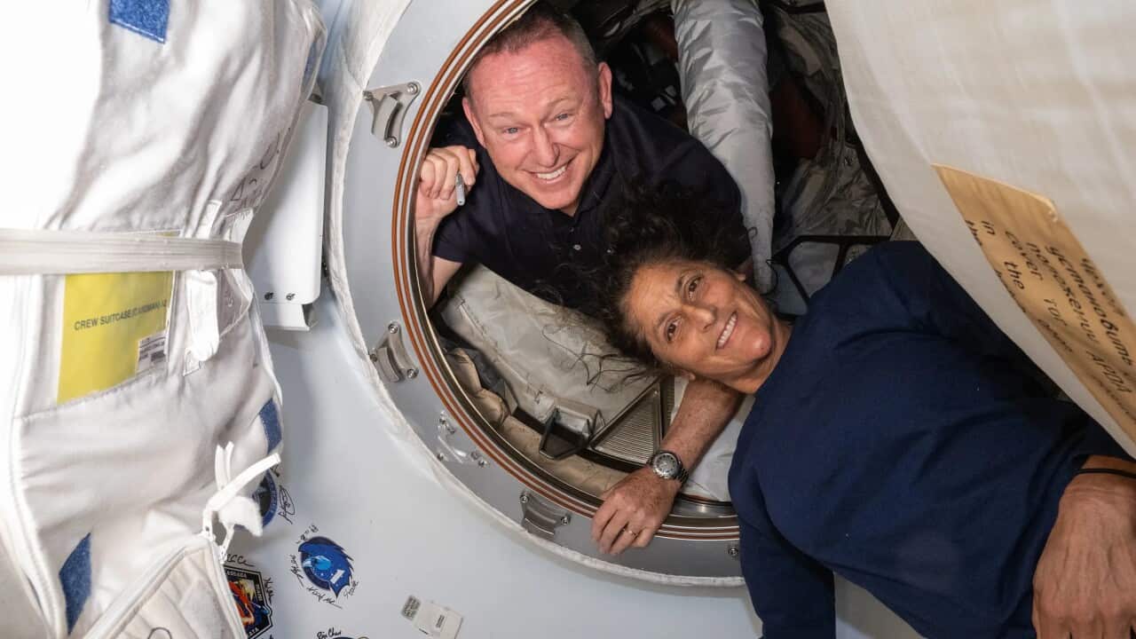 A man and a woman smile inside a spacecraft