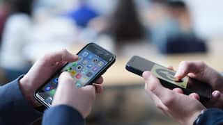 Two school children scrolling on their phones.