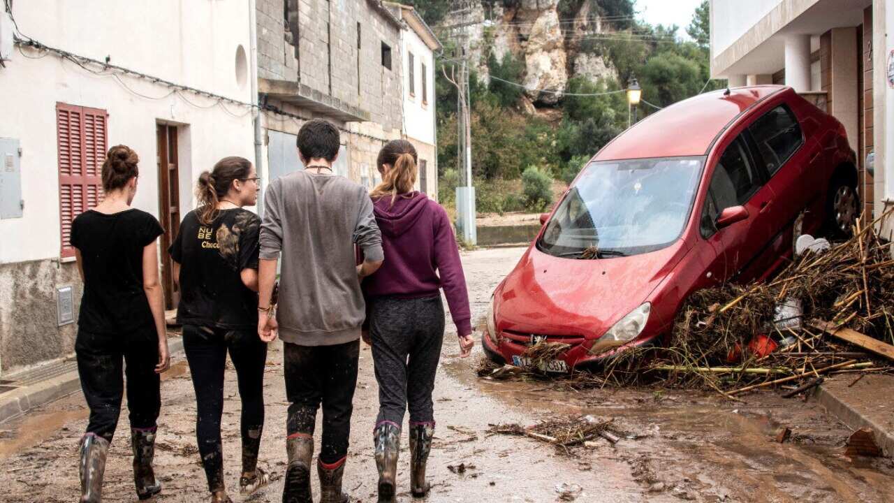 Residents walk along a muddy street during clean-up efforts after flash floods hit Mallorca