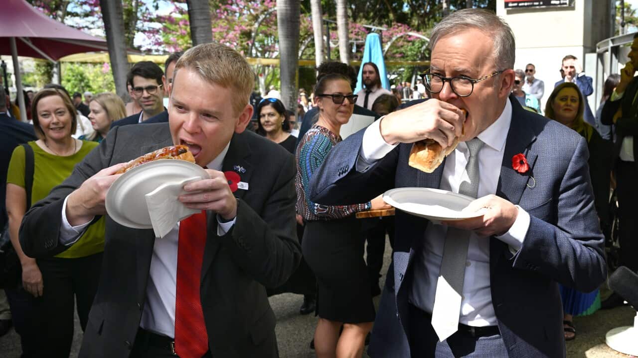 New Zealand Prime Minister Chris Hipkins (left) and Australian Prime Minister Anthony Albanese (right) are seen eating a sausage in a roll at a BBQ.