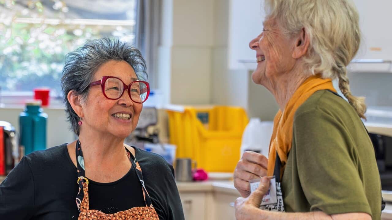 Two women wearing aprons laugh, while standing in a kitchen.