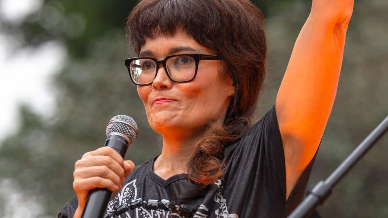 A woman standing on stage holding a microphone with one hand in the air.