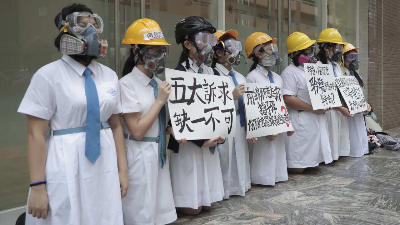 Hong Kong students wearing gas masks and helmets hold a banner which reads "five major demands are indispensable".