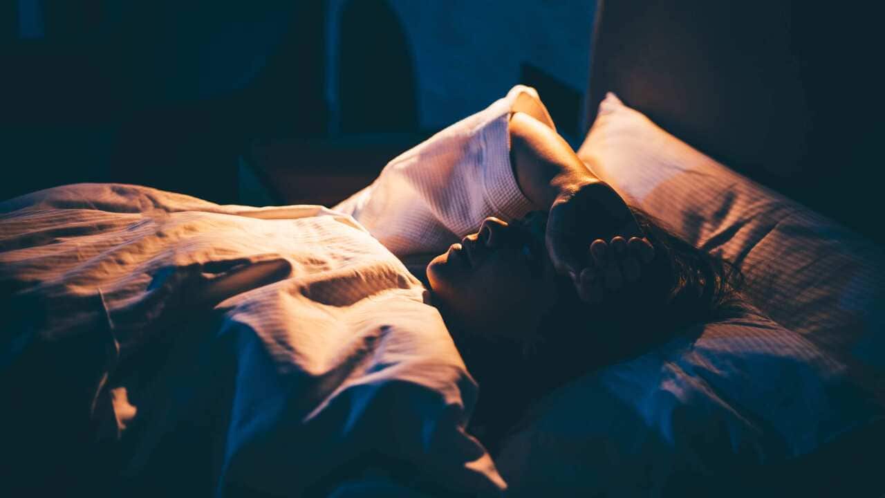 A young woman lying in bed with her hand on forehead.