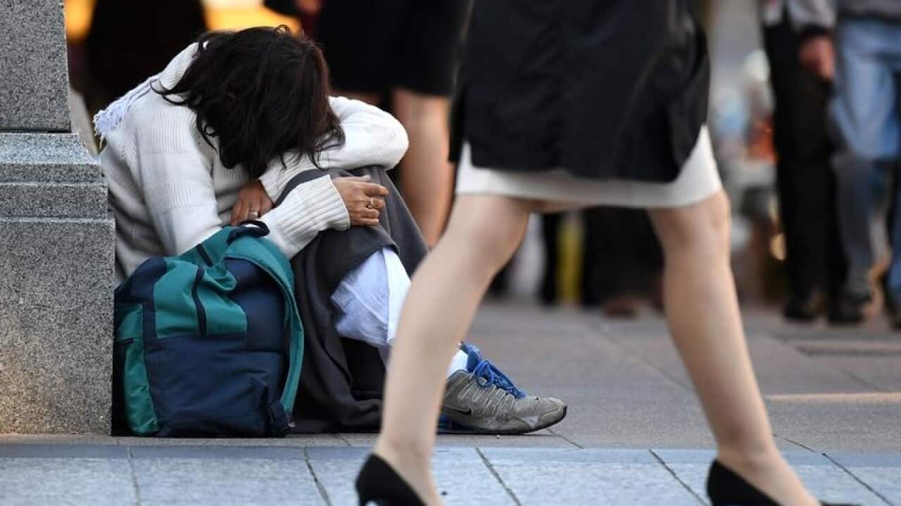 A homeless woman sits on a street corner in Brisbane