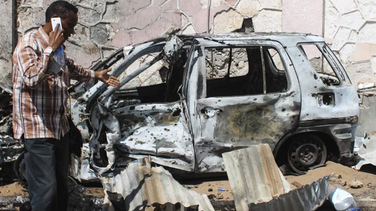 A man walks in front of a destroyed car