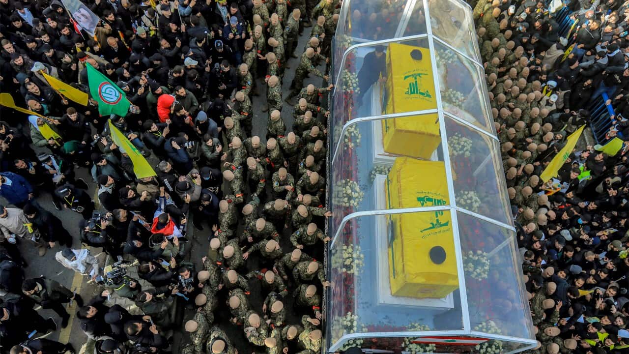 A vehicle carrying two coffins among a crowd at a funeral procession.