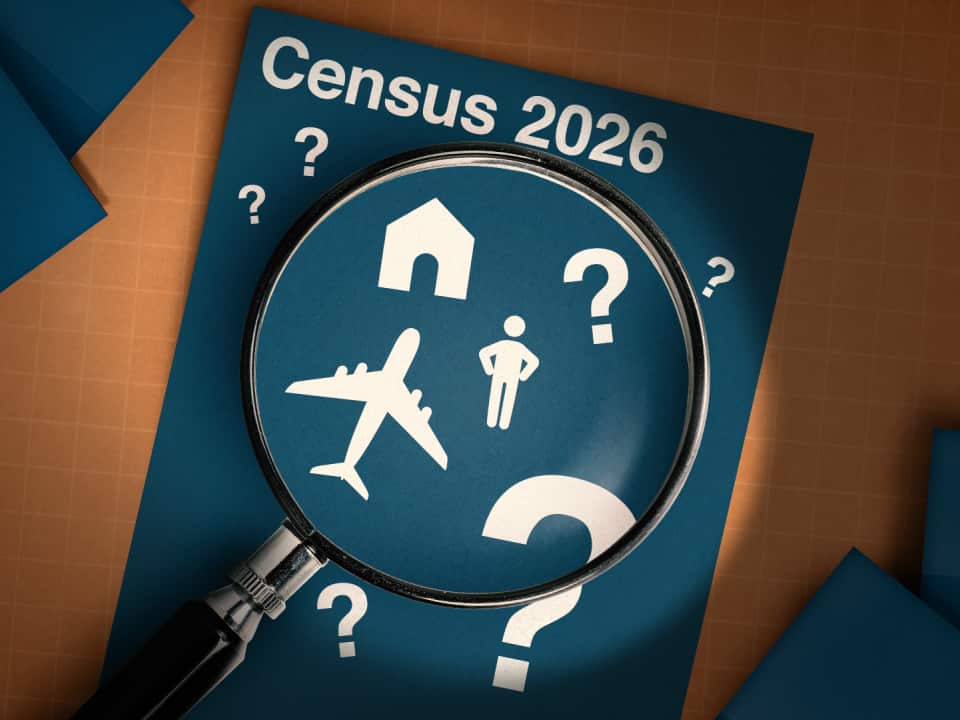 A magnifying glass hovers over a blue piece of paper with various white icons and question marks. The paper includes the text Census 2026.