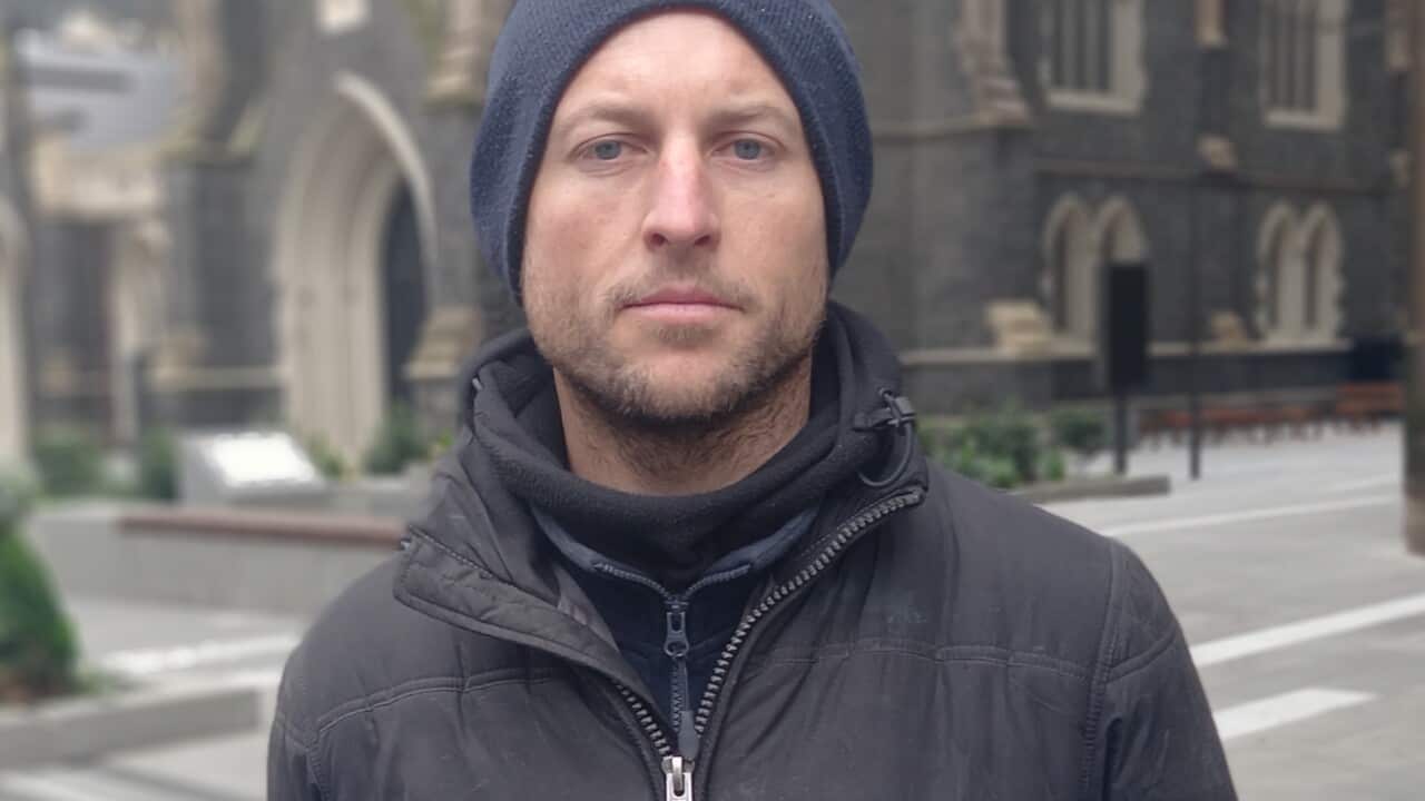 Man wearing a black jacket and beanie standing in front of a church.
