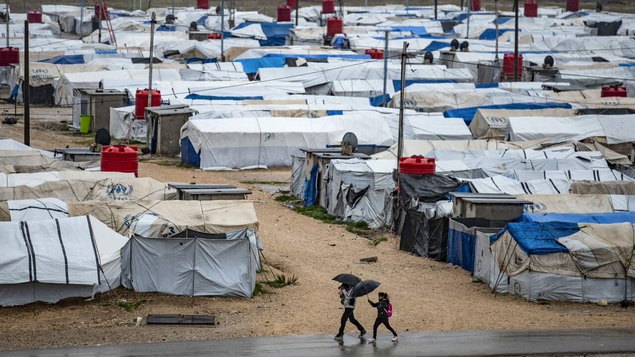 People using umbrellas as they walk outside at a detention camp.