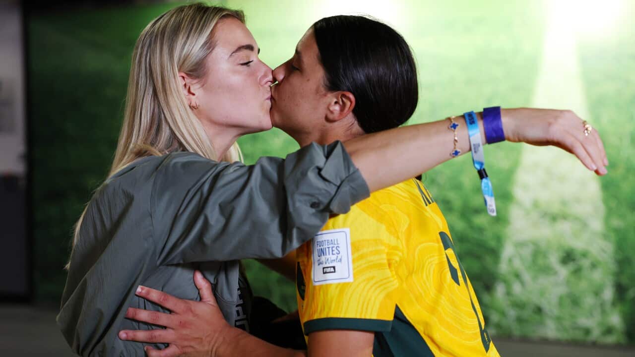 A woman in a grey jacket (left) kisses a woman in a yellow football shirt