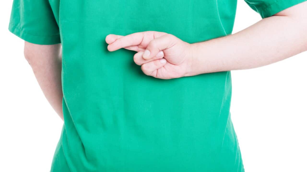 A man in doctor's scrubs crosses his fingers behind his back
