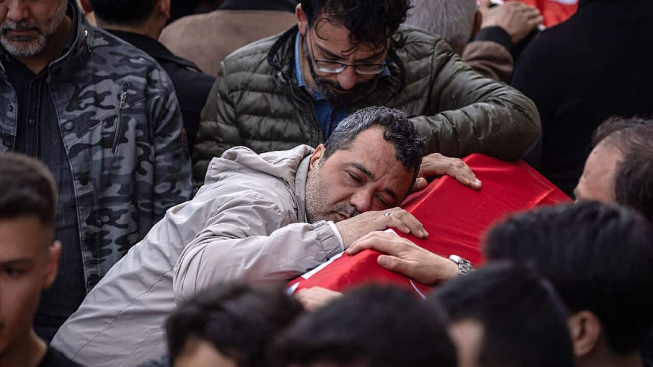 A man grasps a coffin among crowds at a funeral.