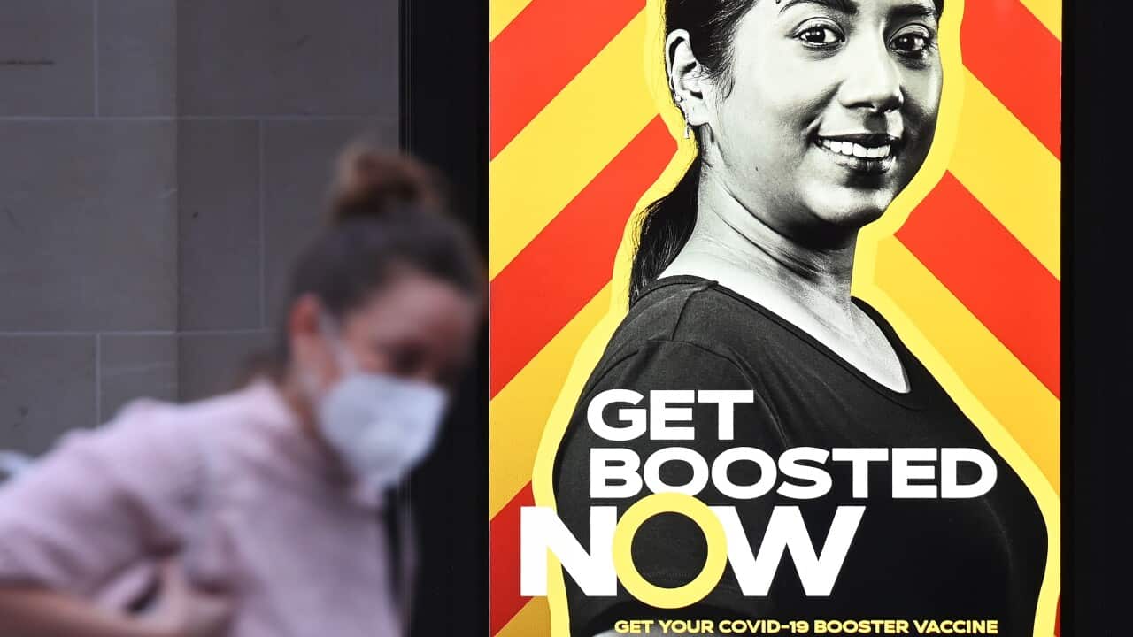 A woman walks past a government COVID-19 vaccine booster campaign advertisement in London, 15 December 2021.